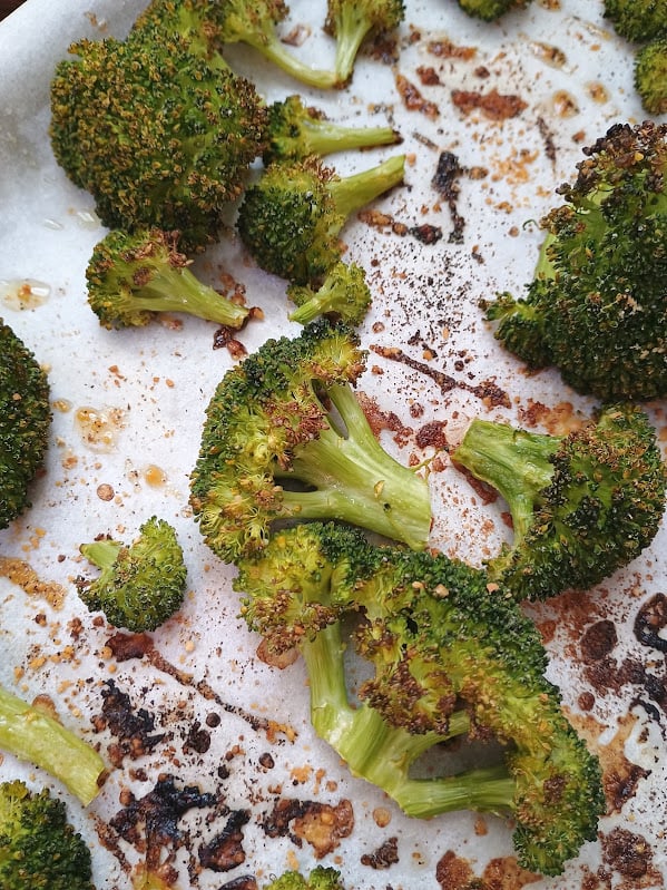 Roasted broccoli florets with browned edges on a parchment lined baking sheet.