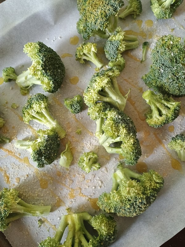 Raw broccoli florets drizzled with olive oil and sprinkled with seasoning before roasting.