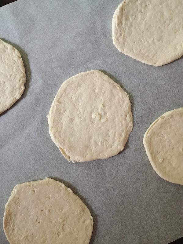 Flattened biscuit dough rounds arranged on parchment paper before adding mini calzone fillings.