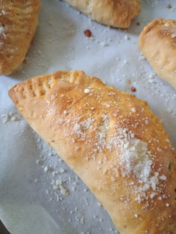 Golden brown mini calzone on parchment paper sprinkled with grated Parmesan.