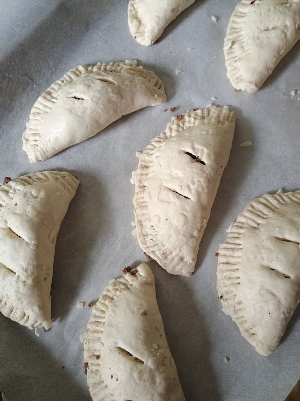 Unbaked mini calzones sealed with fork marks on parchment paper before baking.