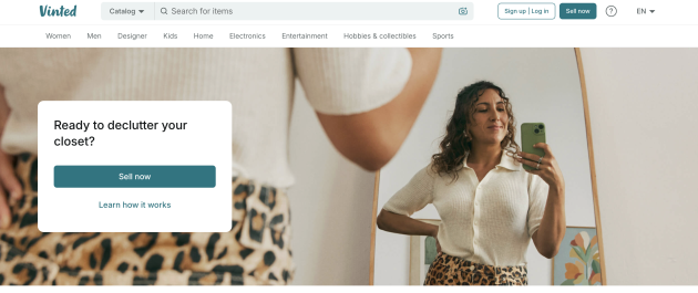 Vinted homepage showing a woman taking a mirror selfie while modeling a white top and leopard print skirt. A "Sell now" button encourages users to list secondhand clothing on the reselling app.