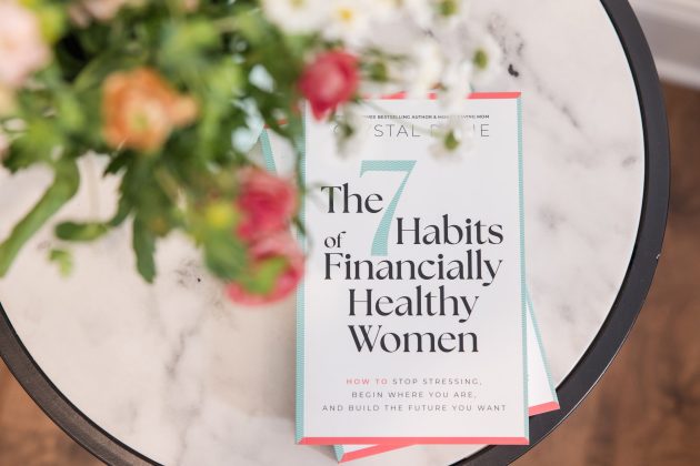 The book "The 7 Habits of Financially Healthy Women" sits on a round marble table beside a colorful bouquet of flowers.