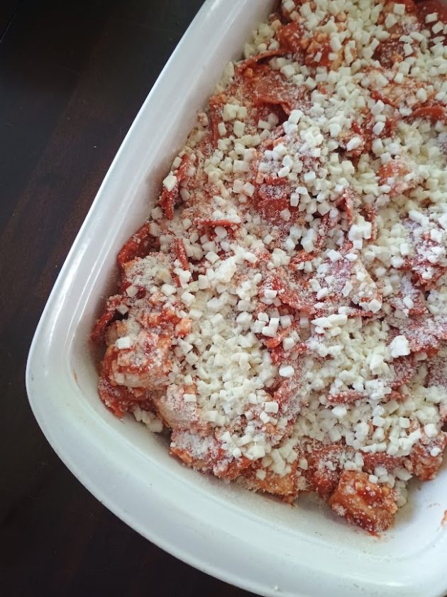 Unbaked bubble pizza in a white casserole dish covered with pepperoni shredded mozzarella and Parmesan cheese.