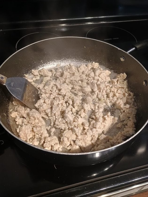 Cooked ground meat crumbled in a large skillet on the stovetop with a metal spatula.