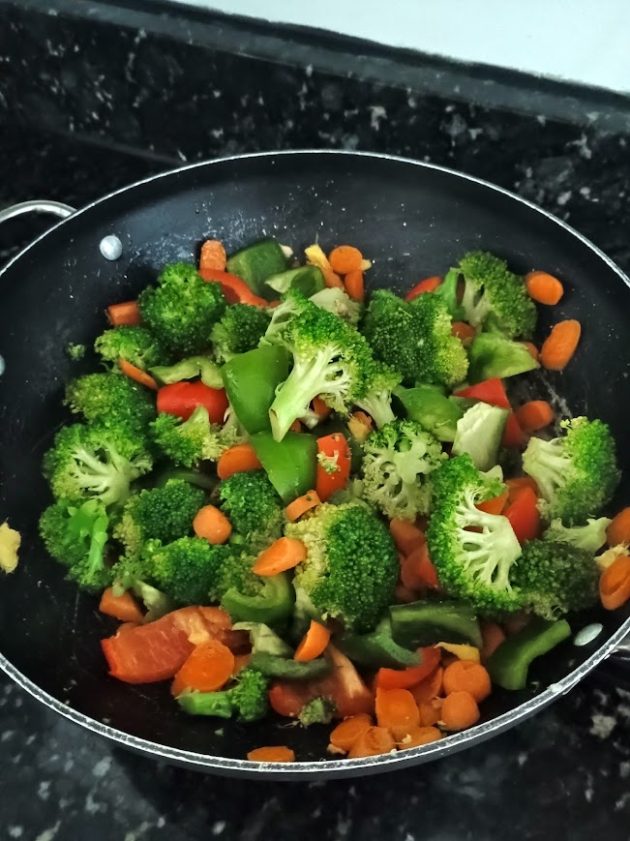 Finished chicken stir fry in a black skillet, with pieces of chicken, broccoli, carrots, red and green bell peppers, and water chestnuts coated in a savory brown sauce.