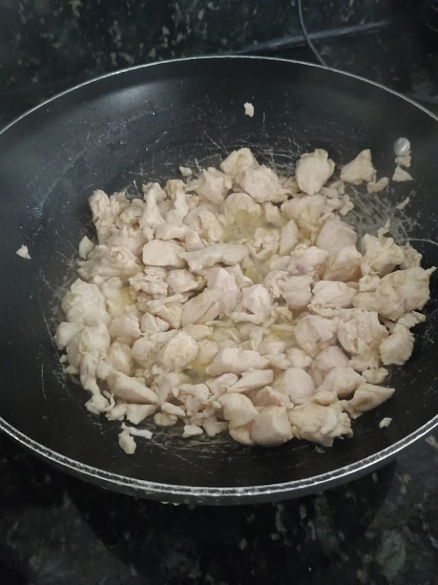 Bite sized pieces of chicken cooking in a black skillet before the vegetables and sauce are added to the chicken stir fry.