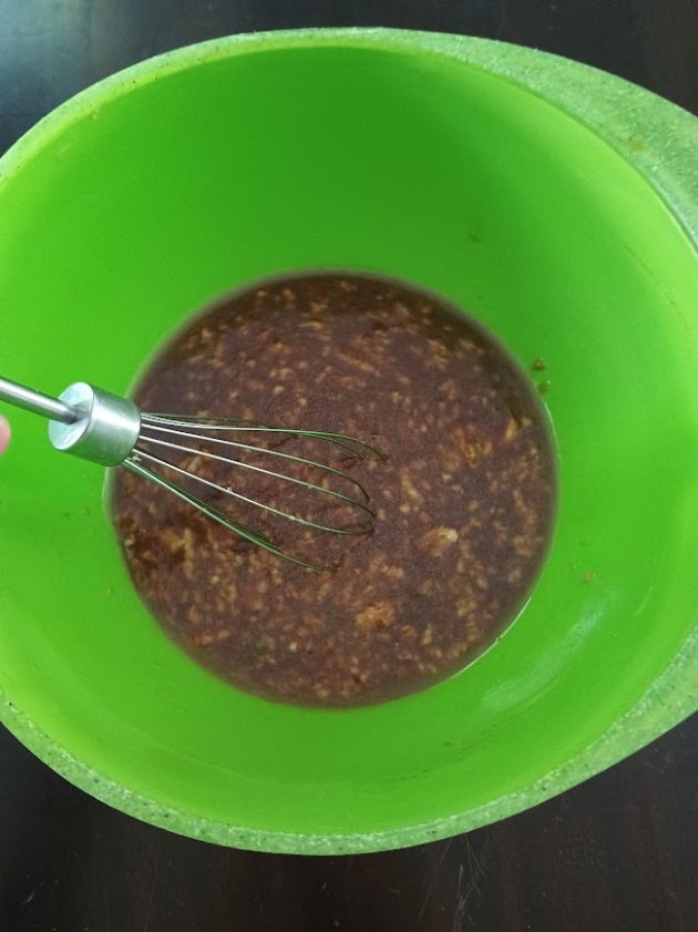 Brown stir fry sauce being mixed with a metal whisk in a bright green bowl before being added to the chicken and vegetables.