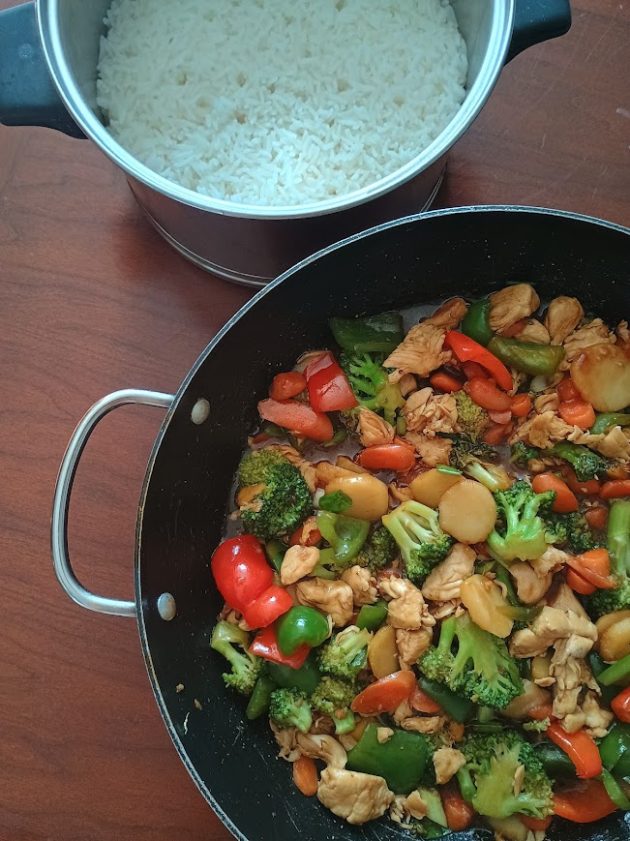 Close up of chicken stir fry showing tender chicken pieces, broccoli florets, sliced carrots, red and green bell peppers, and water chestnuts coated in brown stir fry sauce.